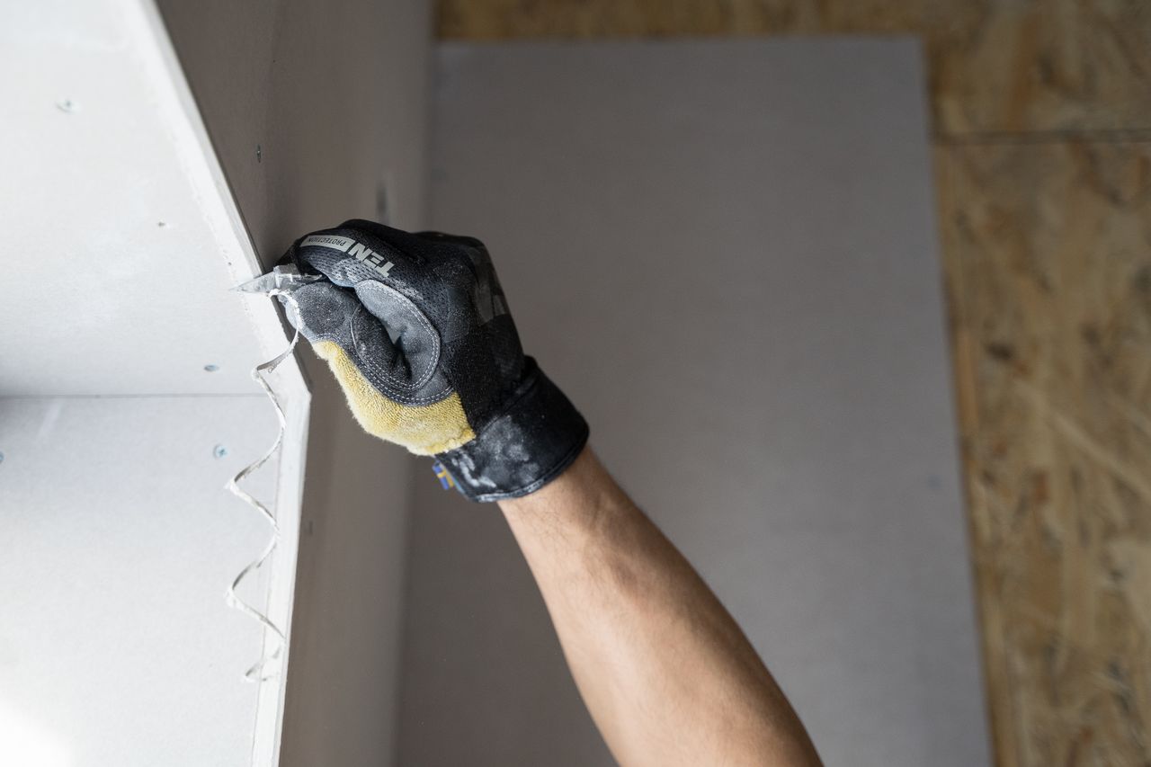 Services Close-up of a gloved hand applying plaster to a wall indoors in Falun, Sweden.
