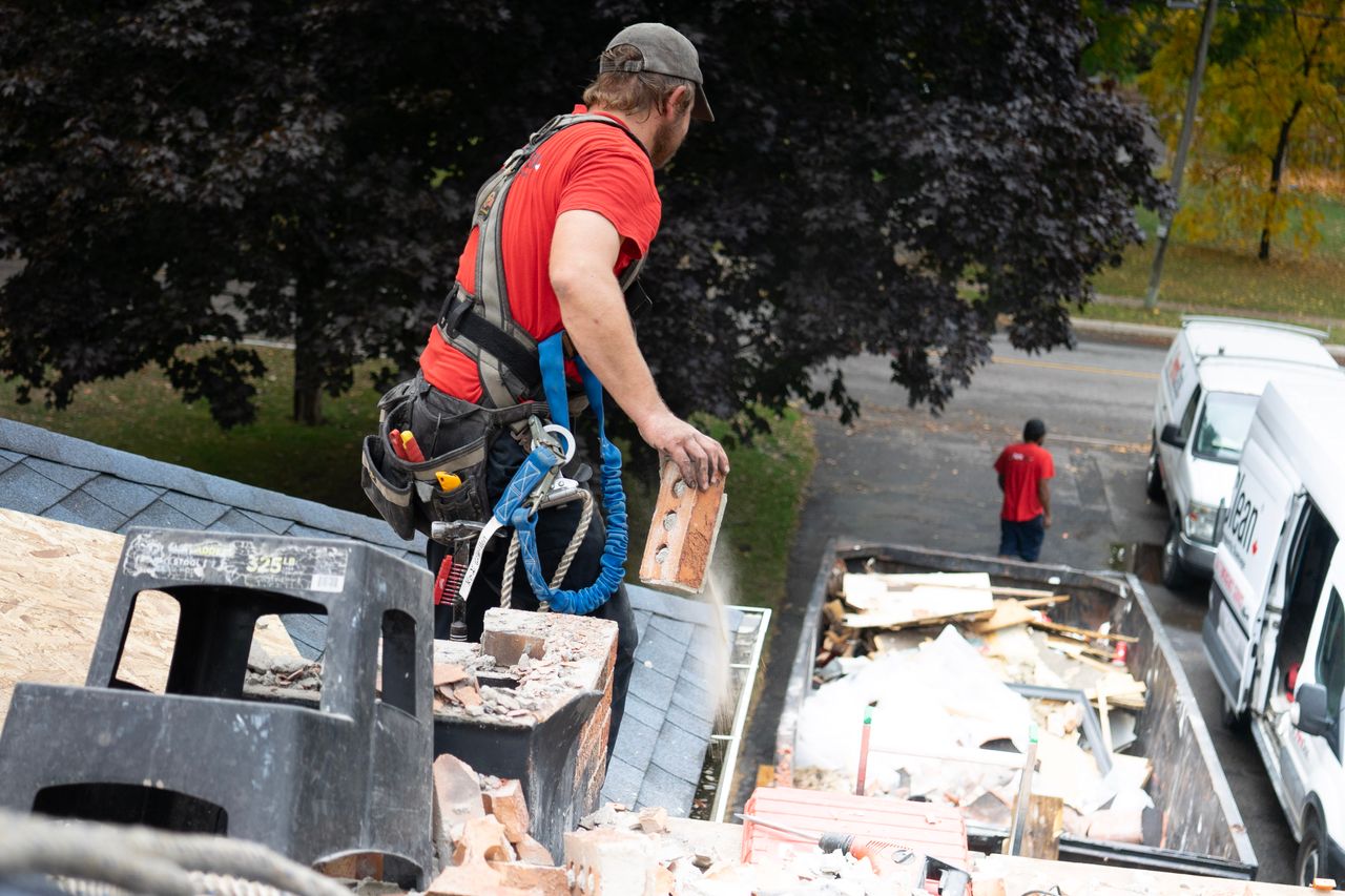 Home Worker in safety harness removes bricks from roof into dumpster below.